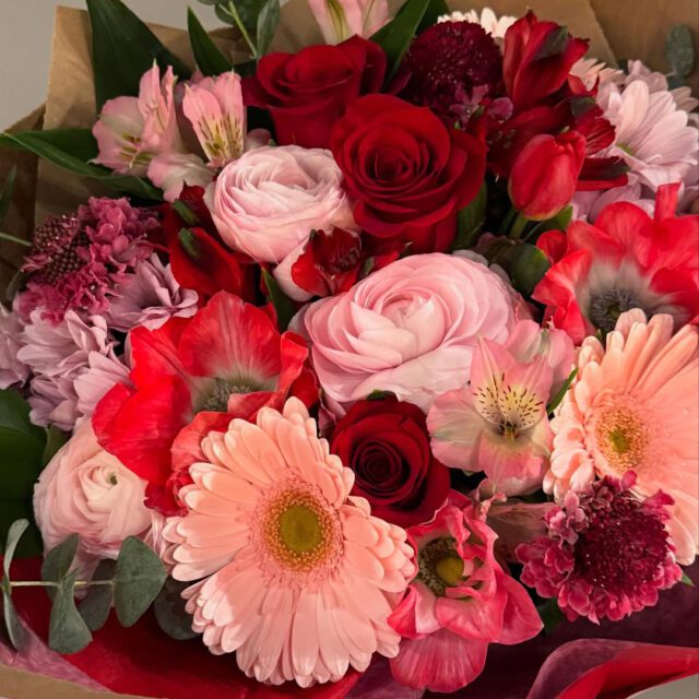 Bouquet de fleurs aux tons rosés et rouges préparé par Fleuriste Centre-Ville au centre-ville de Montréal.