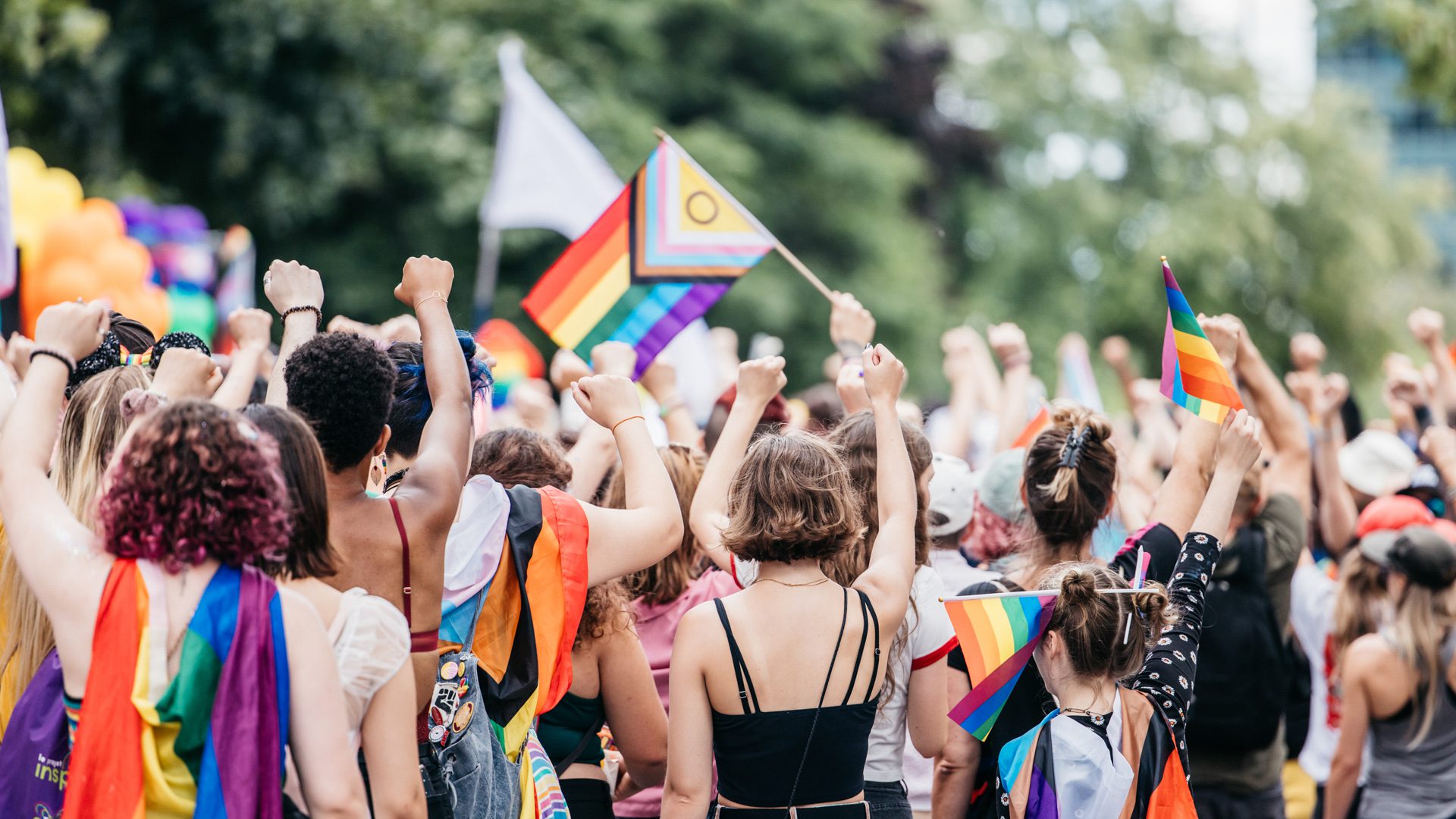 Foule célébrant la Fierté Montréal avec des drapeaux arc-en-ciel et des poings levés.