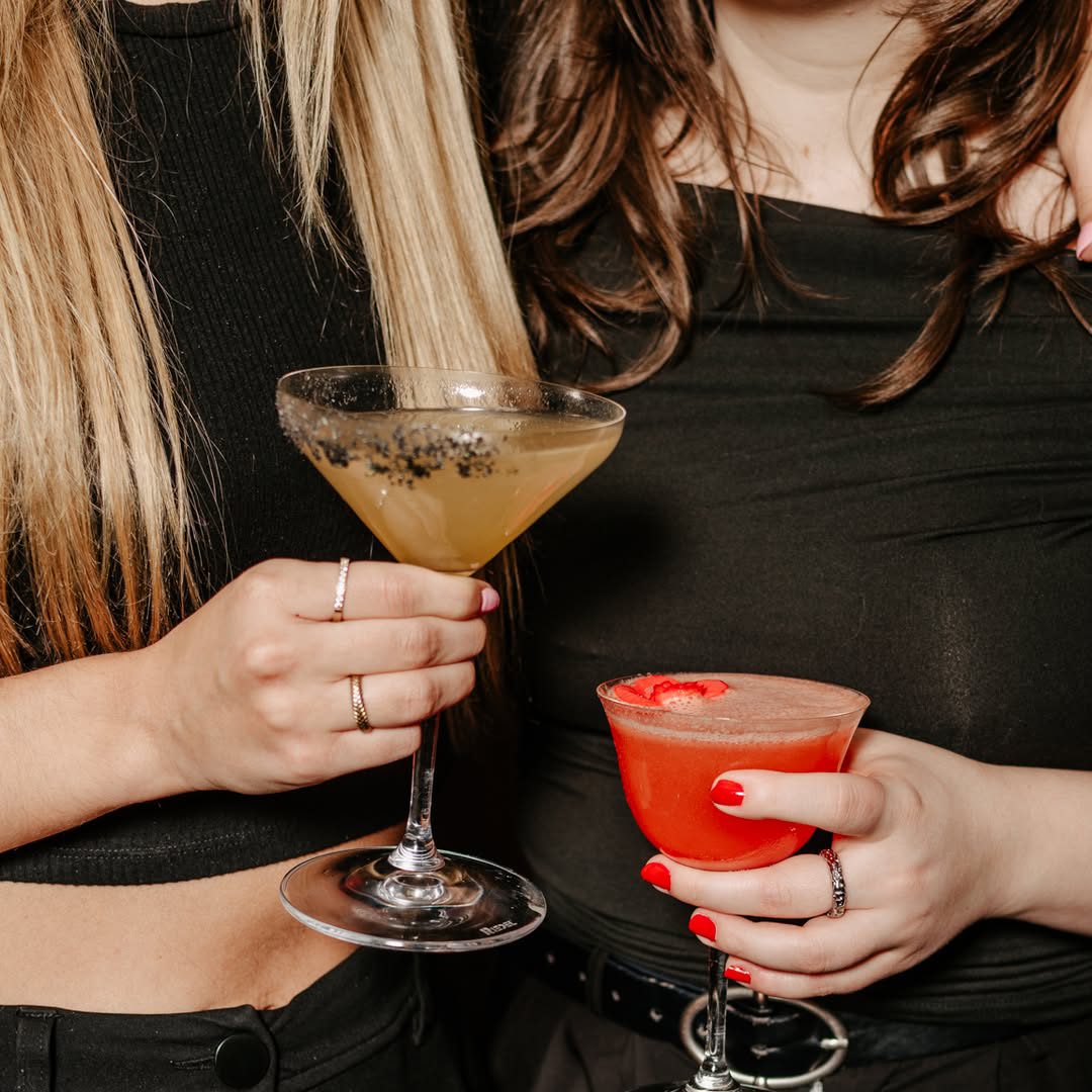Deux femmes tenant des cocktails colorés au H3 lors d’une soirée chic à Montréal, habillées en noir