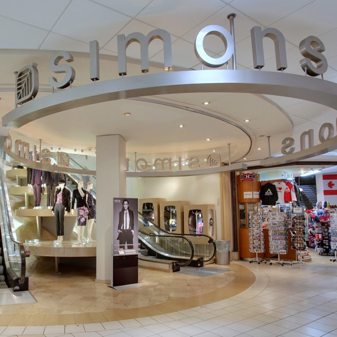 Entrance of Simons at Carrefour Industrielle Alliance in Montreal, showing escalators and clothing displays.