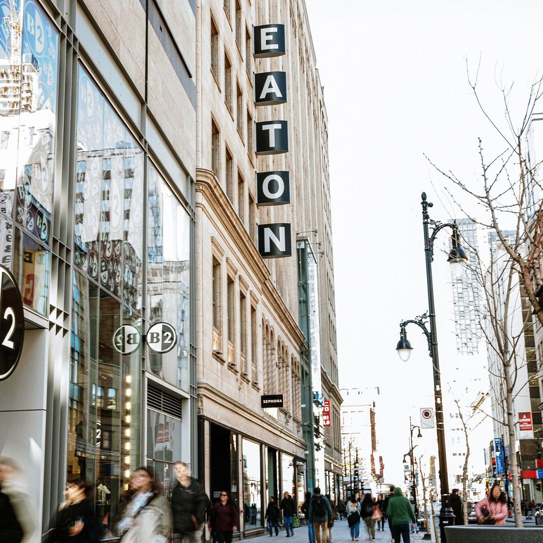 Entrée du Centre Eaton sur la rue Sainte-Catherine, centre-ville de Montréal, avec des piétons et des enseignes de magasins.