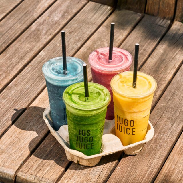 Quatre smoothies colorés Jugo Juice servis à l’extérieur sur une terrasse en bois