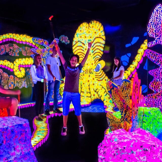 famille jouant au mini-putt fluorescent dans l’univers lumineux du Putting Edge Montréal.