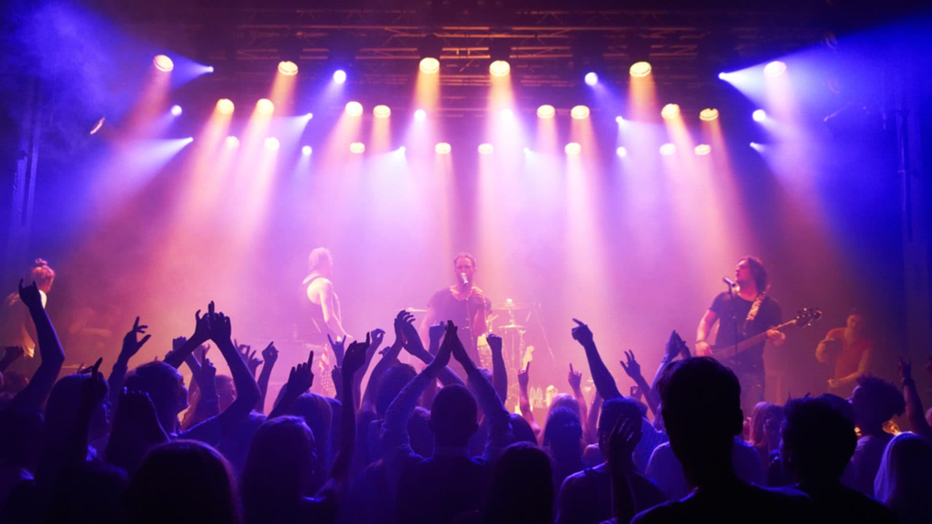 Concert live avec musiciens et public sous lumières colorées.