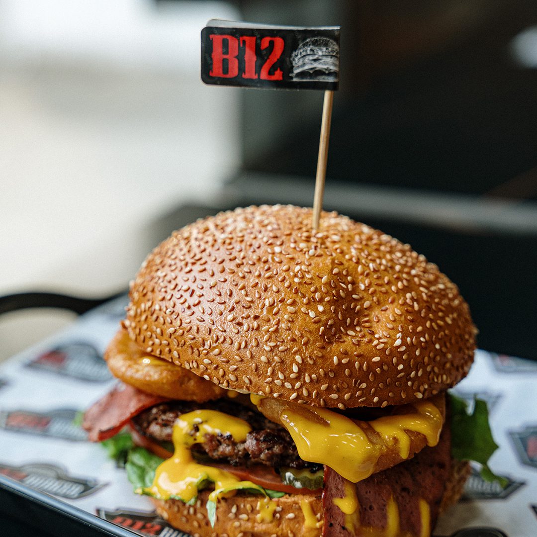 B12 burger with cheese and bacon, topped with onion rings.