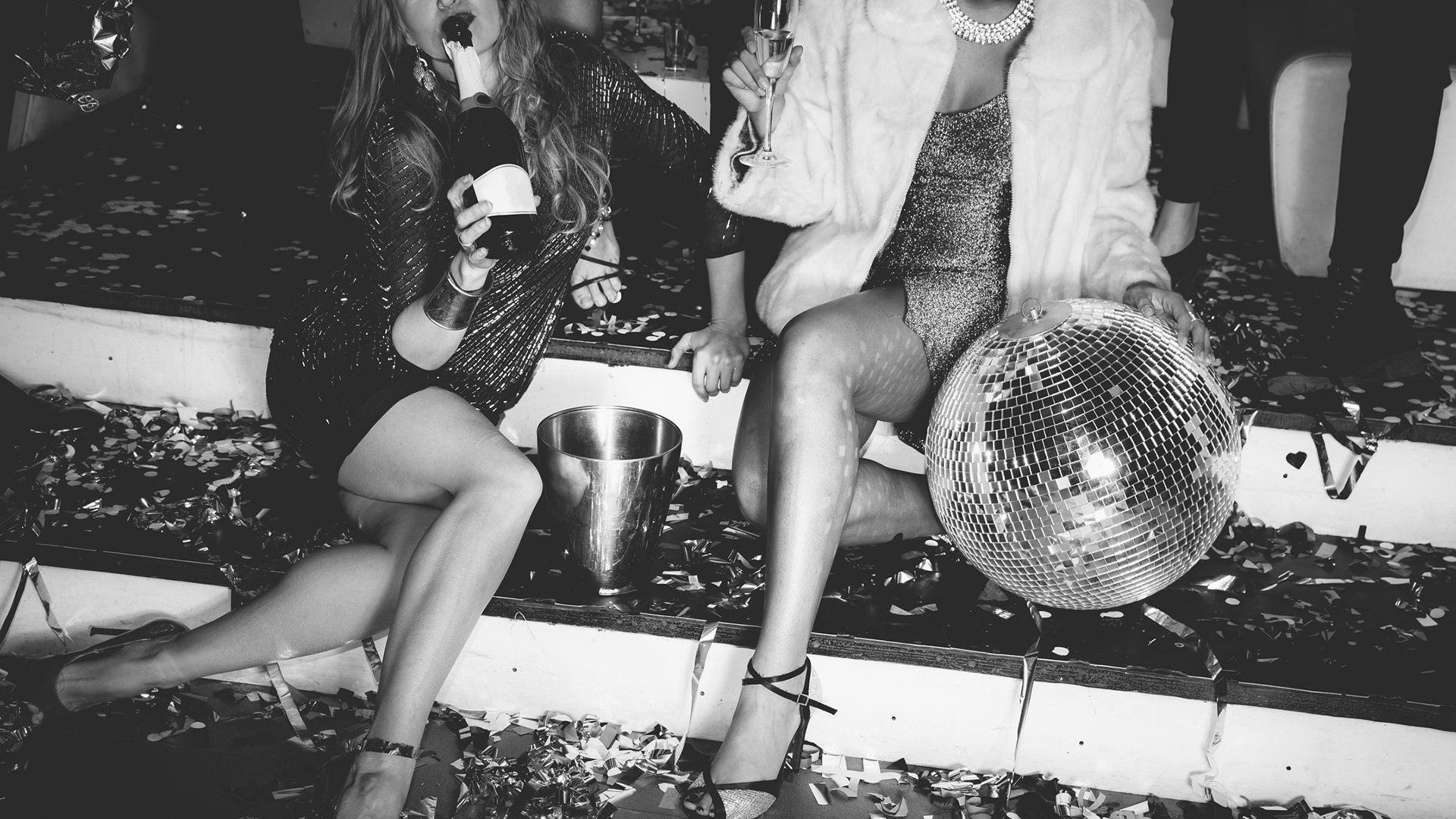 Elegantly dressed people celebrating with champagne and a disco ball at a festive party.