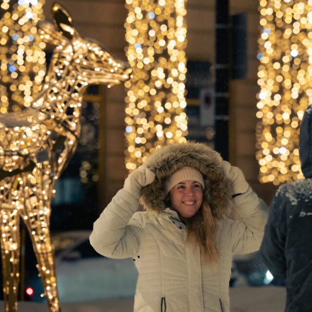 Jeune femme qui sourit et qui se fait prendre en photo devant les illuminations du square Phillips au centre-ville de Montréal