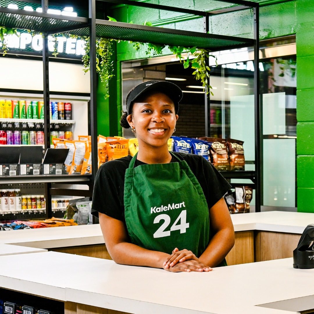 Smiling employee at KaleMart 24 convenience store.