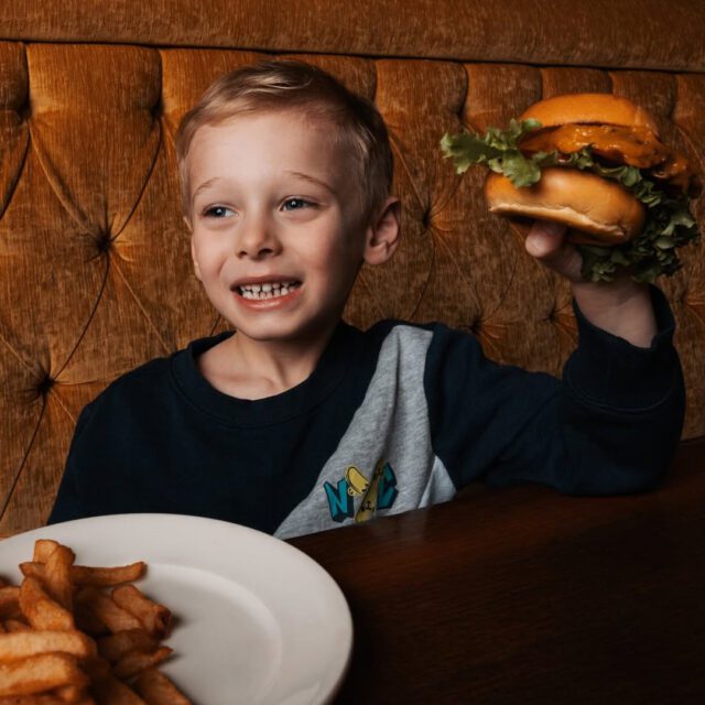 Enfant qui tient un bruger dans ses mains au La Belle et La Boeuf au centre-ville de Montréal