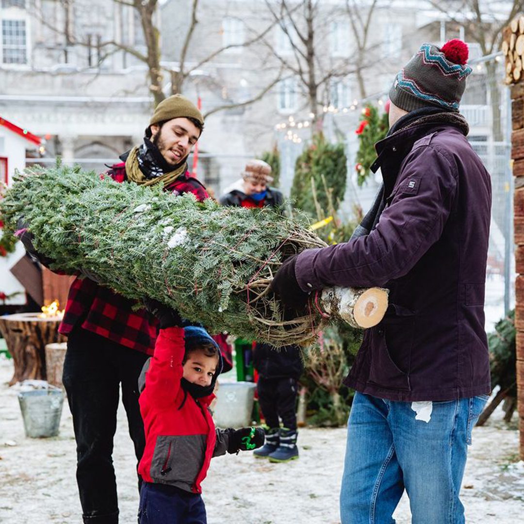 Enfant et adultes portant un sapin sous la neige pendant le Marché de Noël 