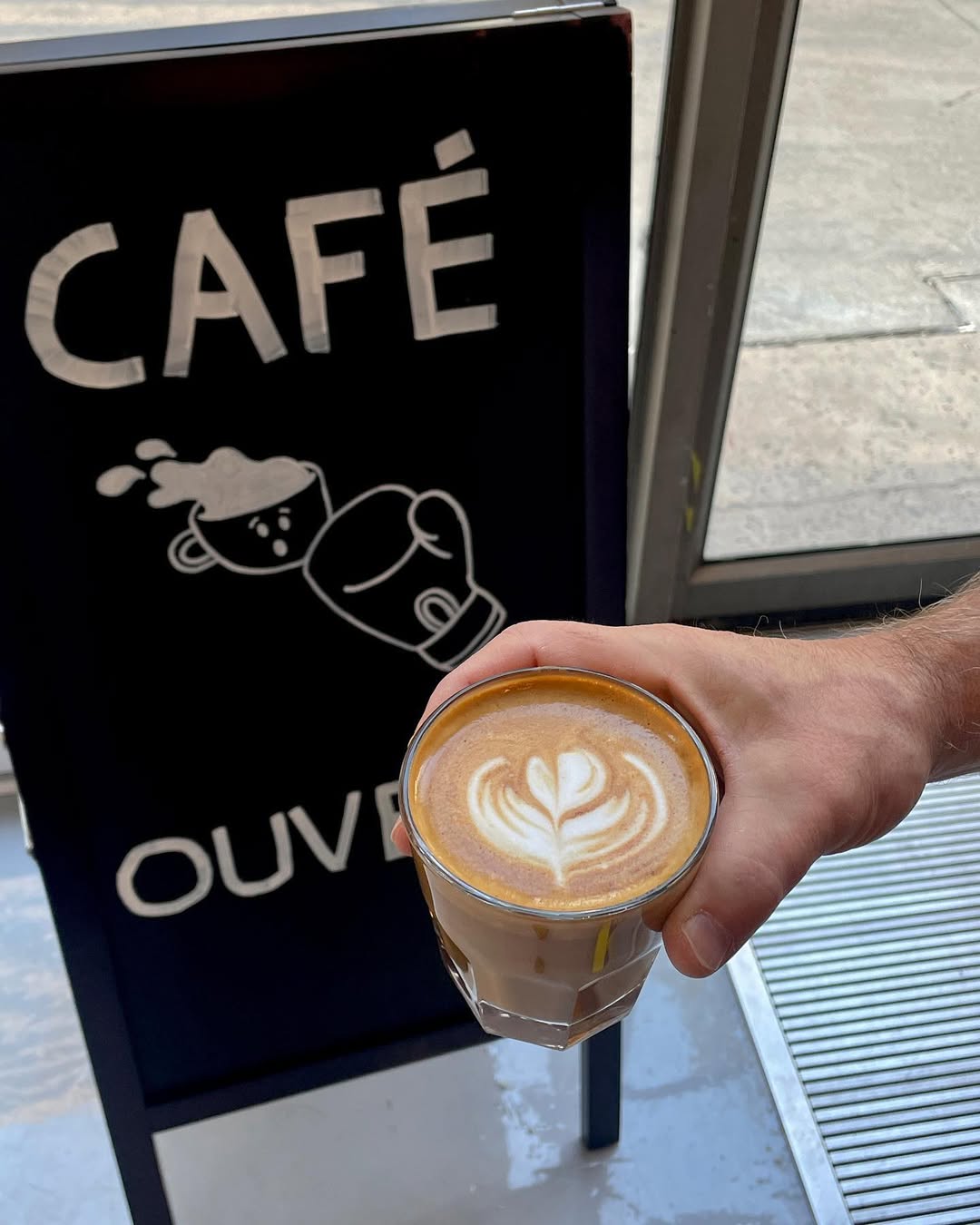 Café latte avec latte art devant l’enseigne du café UpperCup à Montréal.