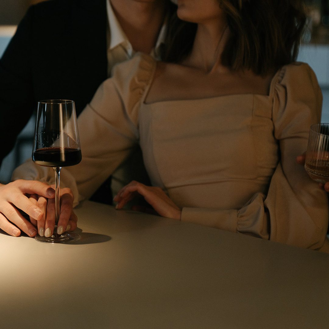 Un couple élégant partage un moment intime autour d’un verre de vin.