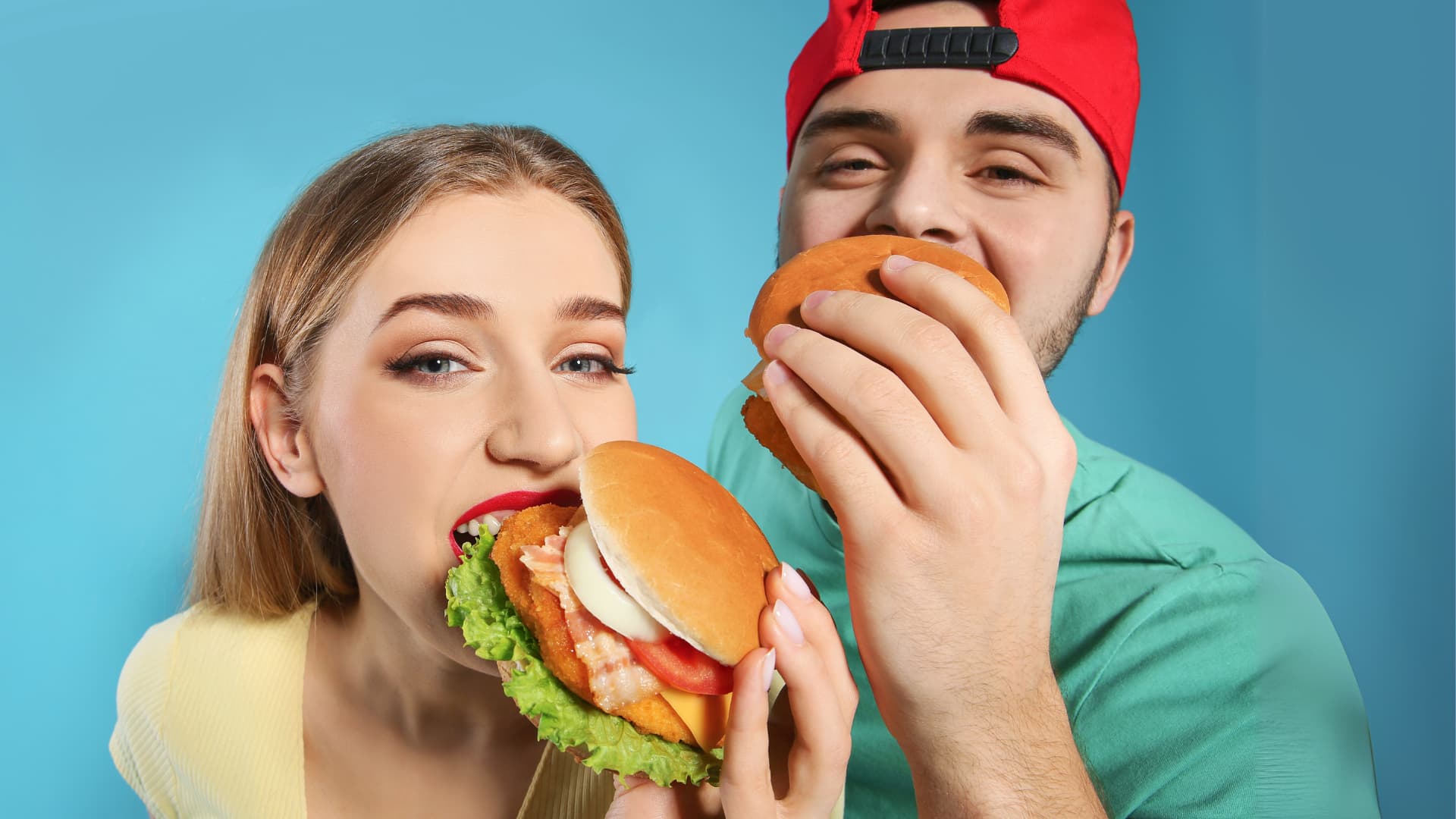 Couple heureux avec une fille et un garçon en train de manger des burgers sur un fond bleu