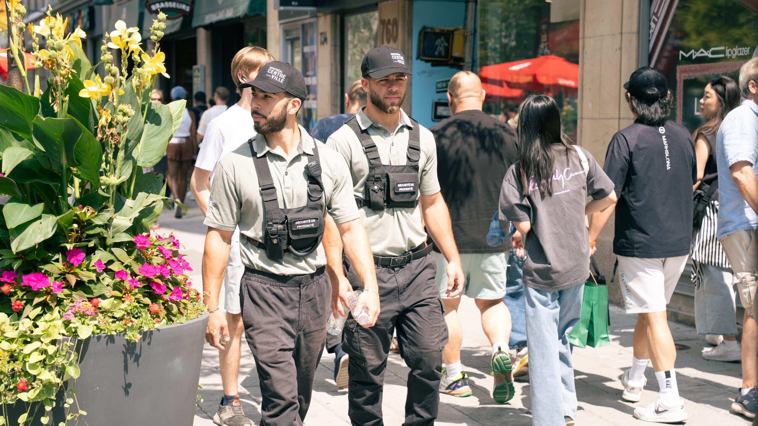 Deux membres de la brigade de sécurité de proximité de Montréal centre-ville marchent sur le trottoir, entourés de passants.