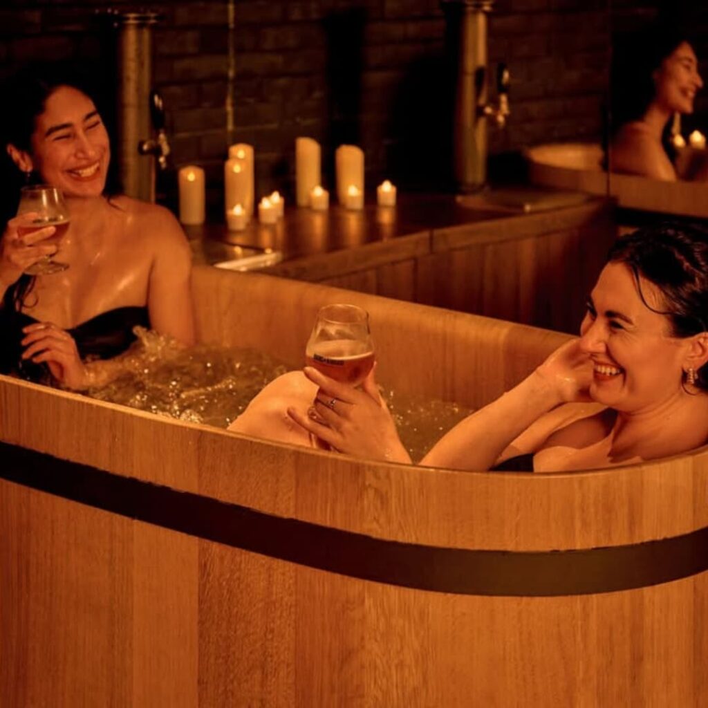 Deux jeunes femmes dans un bain relaxant tenant un verre de bière.